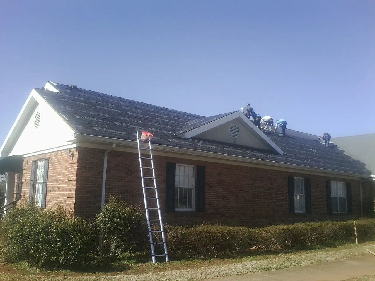 Crew tearing shingles off a brick ranch roof with a ladder set — Metal Roof Repair work by our crew in Yale