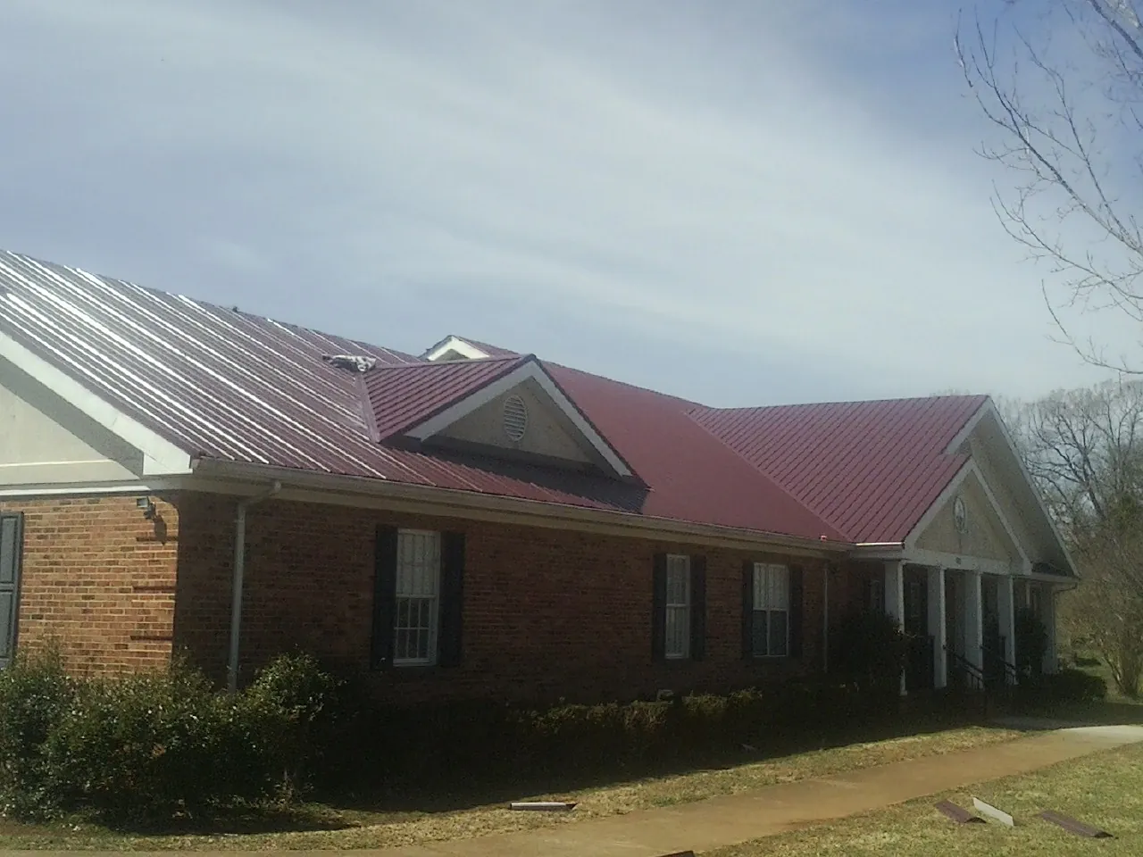 Red metal roof with gabled entries on a long brick building, from a Hail Damage Roof Repair job in Yale