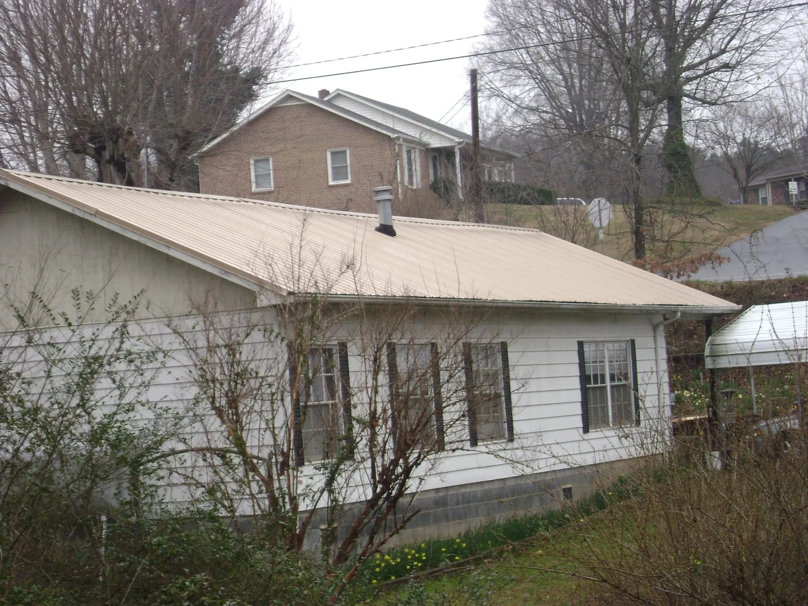 Tan metal roof on a white sided house set into a hillside — Commercial Roofing by Roofing Brothers in Yale