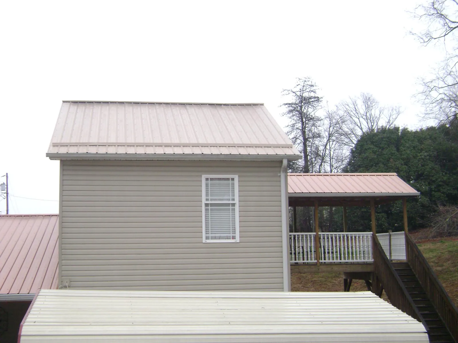 Tan metal roofs on a two story addition and attached porch, from a Roof Replacement job in Yale
